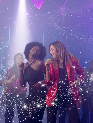 Two women celebrate together at a festive party with vibrant lights | MSC Cruises