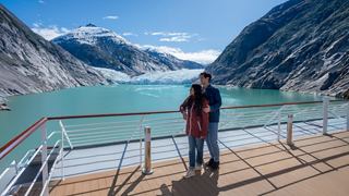 Zwei Menschen auf dem Deck eines Kreuzfahrtschiffs mit schneebedeckten Bergen und See | MSC Cruises