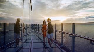 Two people enjoy the sunset on the cruise ship deck with glass railings, Infinity Bridge MSC Seashore | MSC Cruises