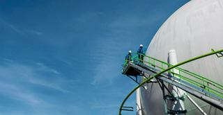 Large white storage tank with green pipes beneath a blue sky in an industrial setting | MSC Cruises