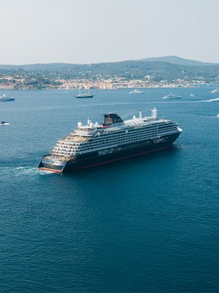 Explora III, ship sails across the blue sea with a distant coastline in view - Explora Journeys