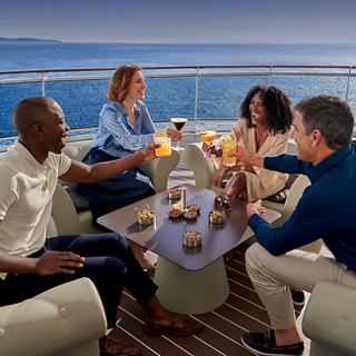 A group of people enjoys drinks and snacks together on a cruise ship deck by the sea | MSC Cruises