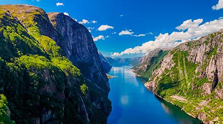 Un paisaje impresionante de un fiordo sereno rodeado de colinas verdes bajo un brillante cielo azul | MSC Cruceros