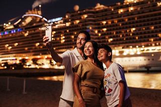 A family takes a selfie at night by the illuminated MSC Seashore ship in the Caribbean | MSC Cruises