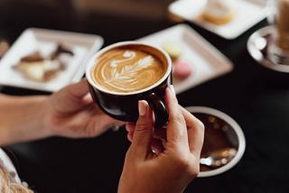 A cup of coffee is held with both hands at a table with dessert plates | MSC Cruises