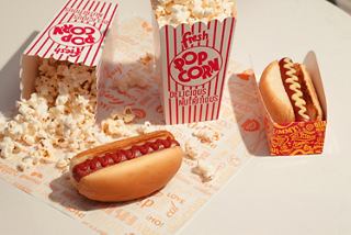 Hot dog with ketchup and mustard beside popcorn containers on a bright background | MSC Cruises