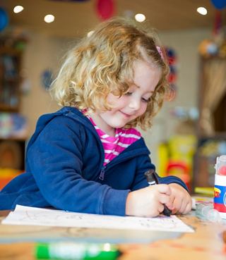 A child with short hair draws with colored pencils at a table surrounded by colorful toys | MSC Cruises