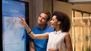 Ein Paar interagiert mit einem interaktiven Display und erkundet gemeinsam begeistert Reiseoptionen | MSC Cruises