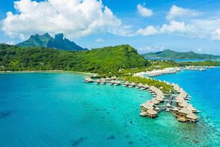 Turquoise lagoon with overwater bungalows set against lush green mountains | MSC Cruises