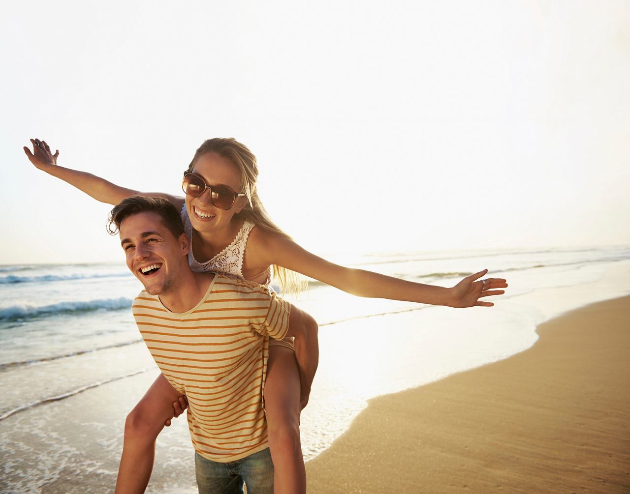 A couple joyfully enjoying a beach day, with one partner playfully carried on the other's back | MSC Cruises