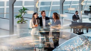 Eine fröhliche Gruppe von drei Freunden genießt eine Mahlzeit zusammen in einem hellen, modernen Speisebereich | MSC Cruises