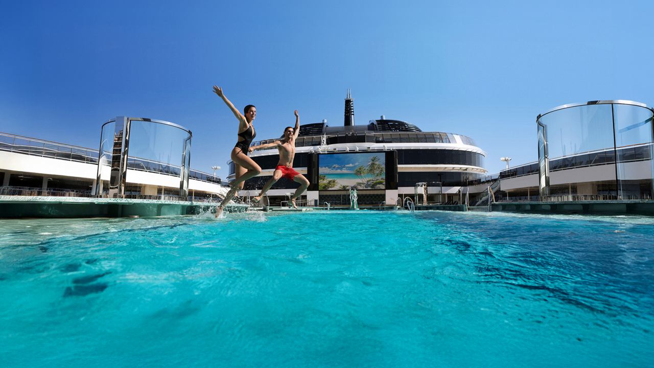 A vibrant pool area with a ship in the background under a clear blue sky | MSC Cruises