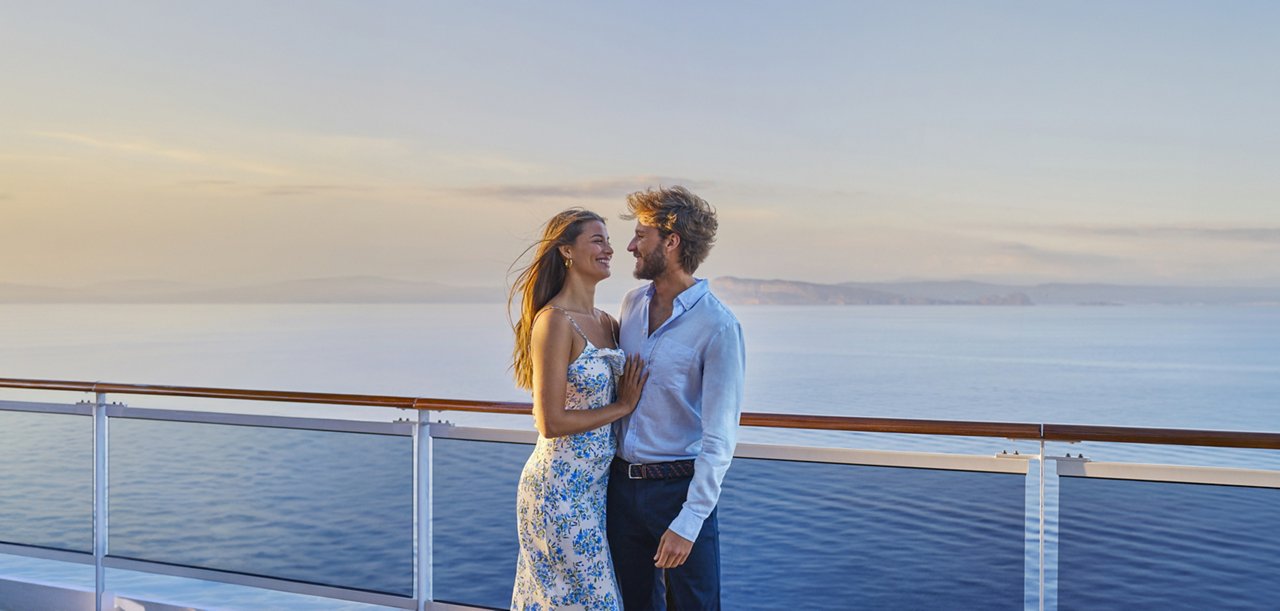 Young man and woman enjoying sea breeze on ship deck with palm trees in the background | MSC Cruises