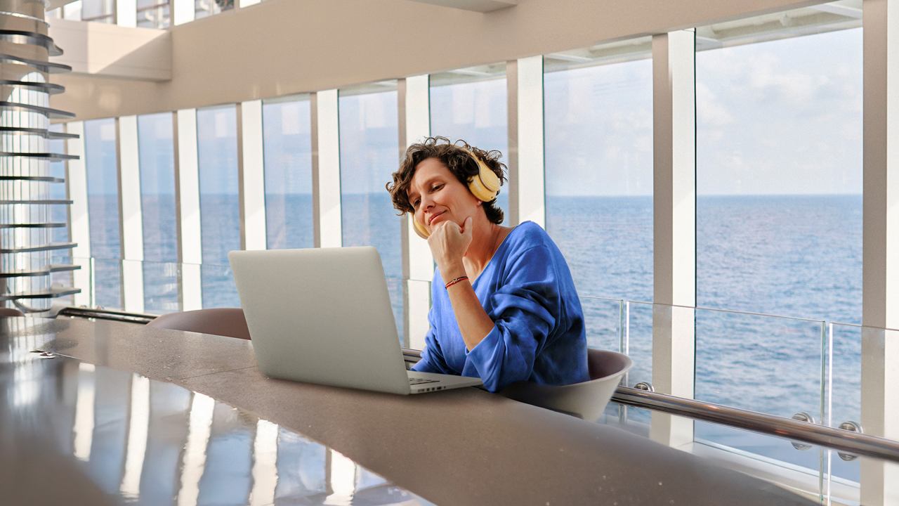 A woman works on her laptop with a sea view, embracing the calmness of her surroundings | MSC Cruises
