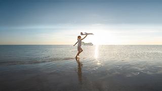 Eine Person geht an einem ruhigen Strand entlang, mit der aufgehenden Sonne im Hintergrund | MSC Cruises
