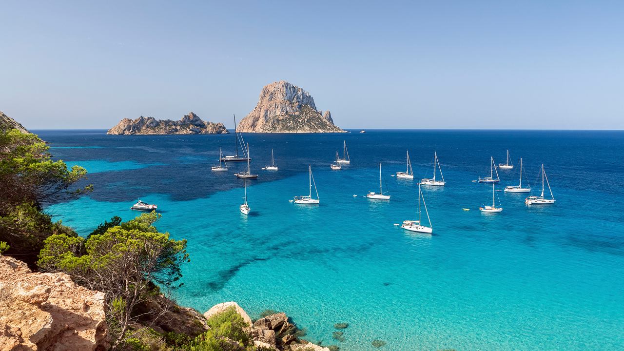 Crystal clear blue water with yachts and a rocky island in the distance | MSC Cruises