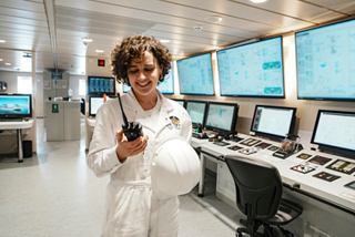 Crew member with radio in the control room of MSC World Europa, surrounded by monitors | MSC Cruises