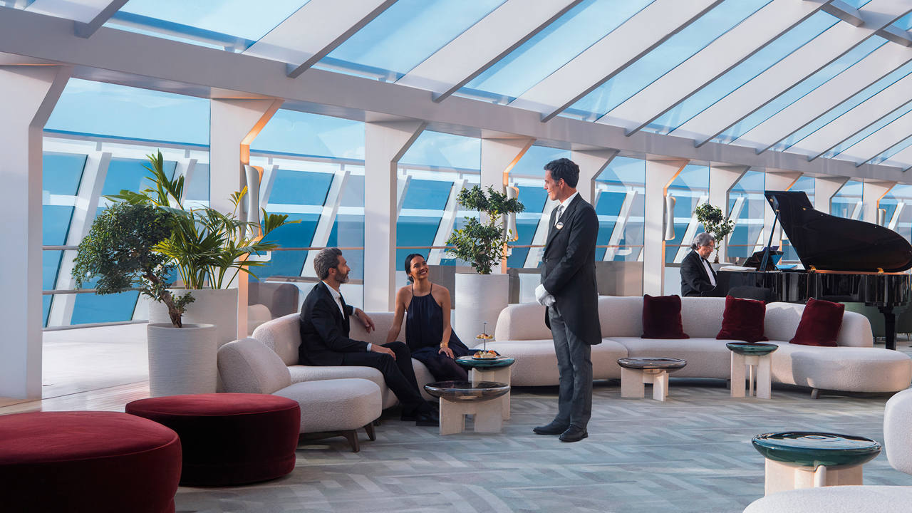 Guests enjoying a luxurious lounge with stunning sea views, accompanied by attentive staff | MSC Cruises