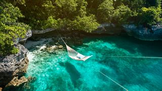 Aerial view of a serene lagoon surrounded by lush vegetation and a person swimming in clear turquoise waters | MSC Cruises