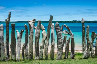 Tall totem poles stand along the shore of Saint-Maurice Bay, with the bright sea and sky in the background | MSC Cruises