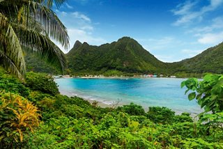 A serene lagoon surrounded by lush vegetation and majestic mountains under a clear blue sky in American Samoa | MSC Cruises