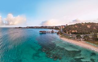 Aerial view of Anse Vata Bay, showcasing the serene sea, beach, and palm trees in Noumea, New Caledonia | MSC Cruises