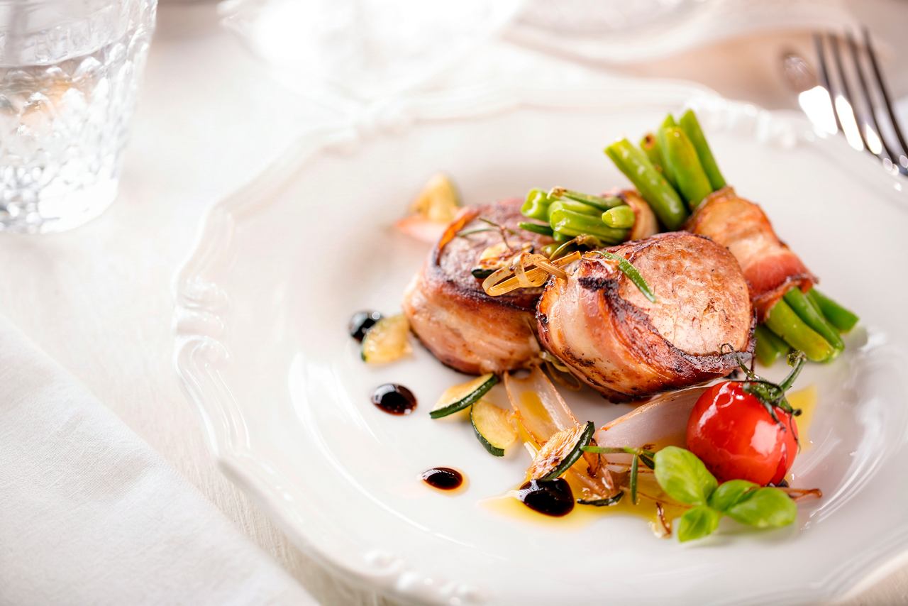 Verre de vin blanc et plat de viande avec tomates au restaurant Posidonia sur MSC Bellissima | MSC Cruises