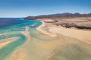 Expansive sandy beach with turquoise waters and mountains at Fuerteventura, Spain | MSC Cruises