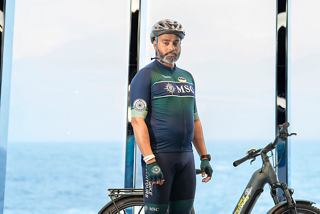 A bike tour leader stands beside a bicycle with a ship and sea in the background | MSC Cruises