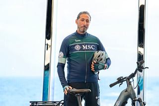 Crew member leading bike tour in front of MSC Euribia with sea and sky in background | MSC Cruises