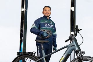 Happy MSC Euribia crew member with bike on deck with sea and sky in the background | MSC Cruises