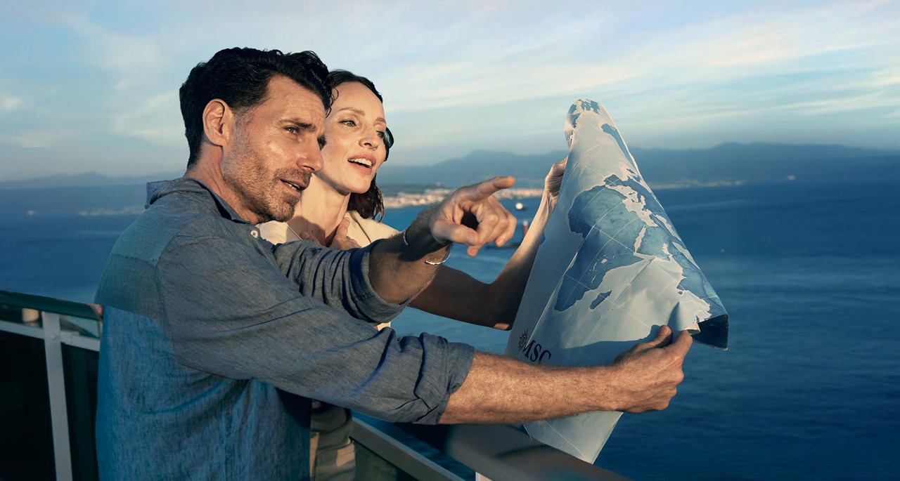 Ein Paar lächelt, während es eine Karte vor der Kulisse des Ozeans betrachtet | MSC Cruises