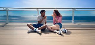 Zwei junge Menschen genießen die Sonne und das Meer, während sie auf dem Deck eines Kreuzfahrtschiffes sitzen | MSC Cruises