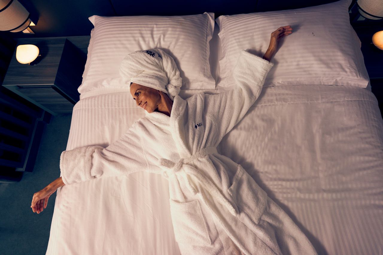 Eine Person in weißem Schlafanzug liegt auf weißen Laken und genießt eine gemütliche Atmosphäre | MSC Cruises