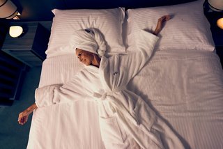 A person in white pajamas lies on white sheets, enjoying a cozy atmosphere | MSC Cruises