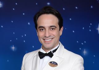 Smiling man in a white suit and bowtie against a starry background | MSC Cruises