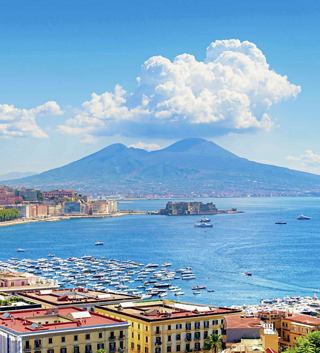 A panoramic view of Naples with Mount Vesuvius in the background and boats in the Gulf | MSC Cruises