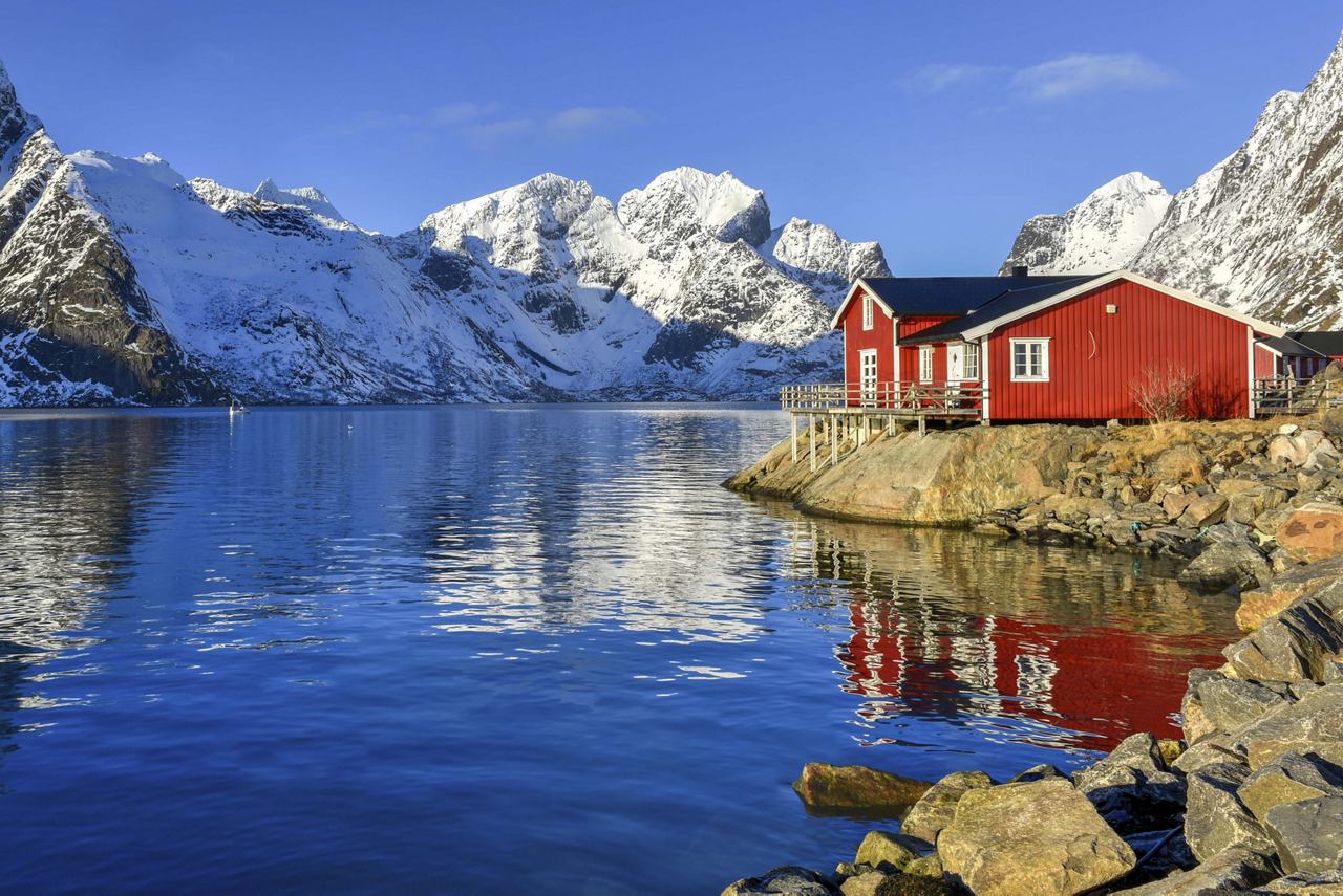 Une scène tranquille d'un chalet rouge au bord d'un lac serein, avec des montagnes enneigées en arrière-plan | MSC Croisières