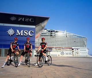 Three staff members in uniform pose outside a modern building with the MSC logo, ready to welcome guests | MSC Cruises