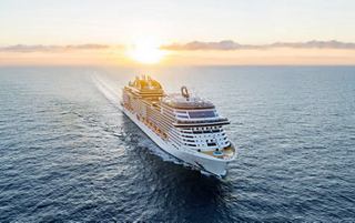 A cruise ship sailing on calm waters with the sun rising in the background | MSC Cruises