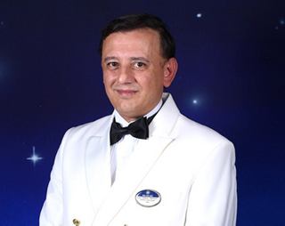 Crew member in white formal uniform with name badge and bow tie | MSC Cruises