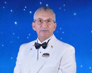 Crew member in white formal uniform with name badge and bow tie | MSC Cruises