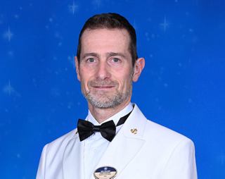 Crew member in white formal uniform with name badge and bow tie | MSC Cruises