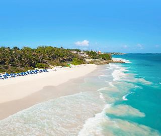 A pristine white sand beach meets crystal blue waters on a sunny day | MSC Cruises