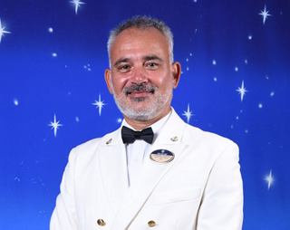 Captain in a white uniform smiling against a starry background | MSC Cruises
