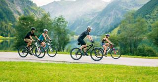 Eine Familie genießt eine malerische Radtour durch üppiges Grün mit Bergen und einem See im Hintergrund | MSC Cruises