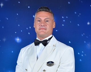 Captain Danilo Cha stands confidently in a formal white suit against a starry blue background | MSC Cruises