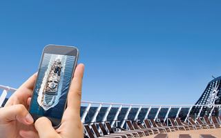 A hand holds a smartphone with a clear blue sky and cruise ship structure in the background | MSC Cruises