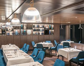 Restaurante espacioso con sillas azules y mesas elegantes, listo para cenas agradables | MSC Cruceros