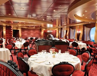 Elegante área de comedor con mesas redondas y decoración de terciopelo rojo, creando un ambiente cálido y acogedor para los huéspedes | MSC Cruceros